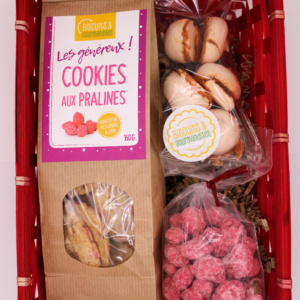 Un coffret dans son panier rouge contenant un paquet de cookie au praline, des meringue ainsie qu'un sachet de praline rose