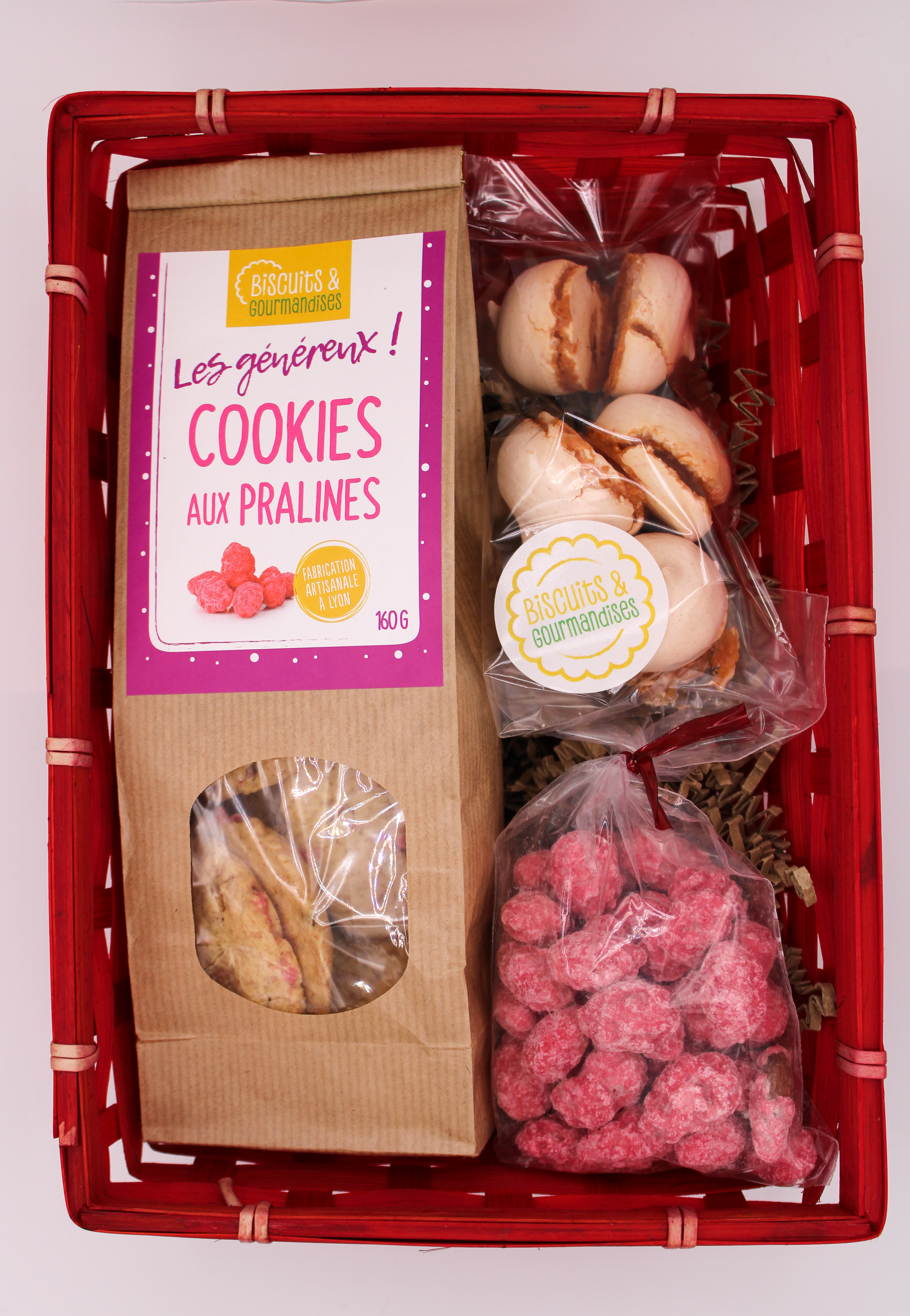 Un coffret dans son panier rouge contenant un paquet de cookie au praline, des meringue ainsie qu'un sachet de praline rose